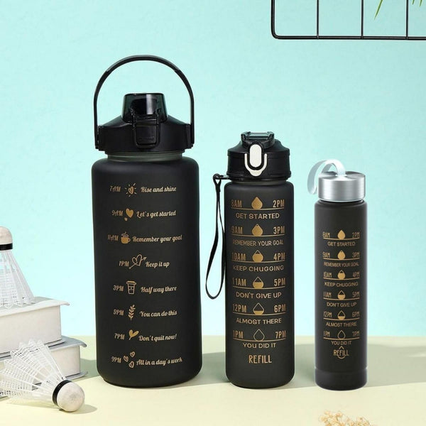 Three black insulated water bottles with gold motivational text and icons, displayed on a light beige surface against a pale blue background.