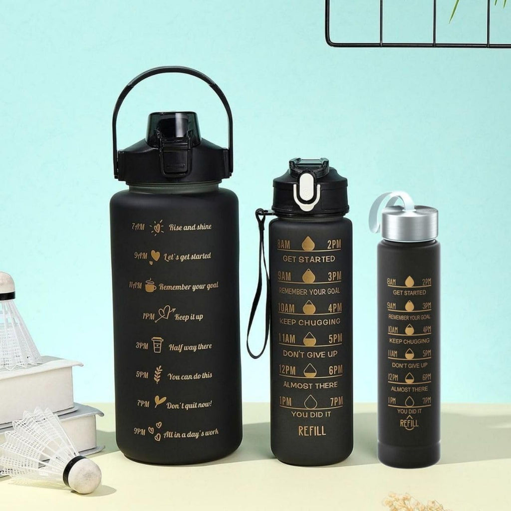 Three black insulated water bottles with gold motivational text and icons, displayed on a light beige surface against a pale blue background.