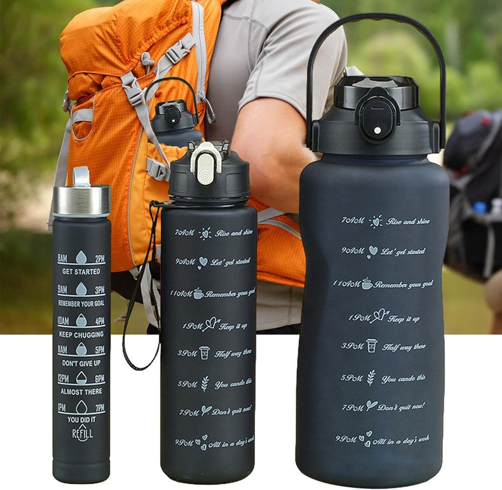 Three reusable water bottles shown in a composite outdoor scene with a person wearing an orange hiking backpack. The bottles are matte black with white printed motivational text and icons; one bottle has a silver cap, one has a white cap, and one has a black handle.