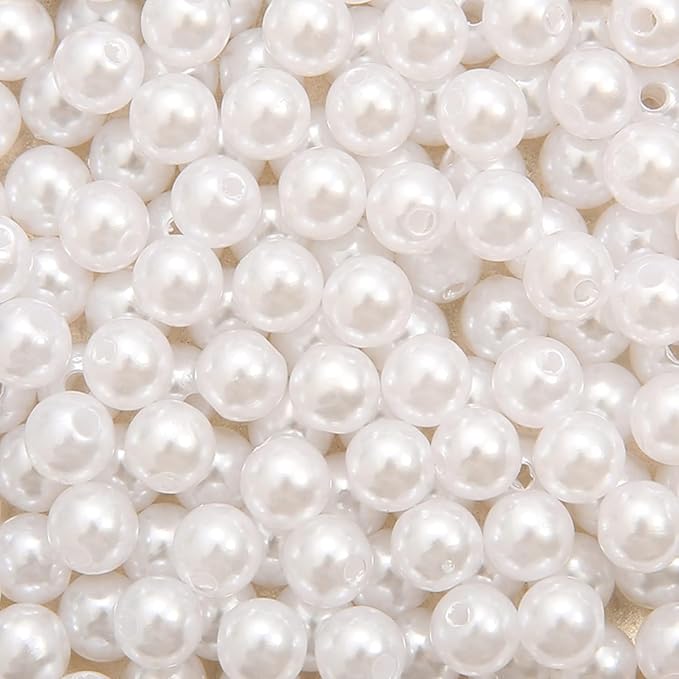 A close-up pile of round, glossy white faux pearl beads with small holes, filling the entire frame.