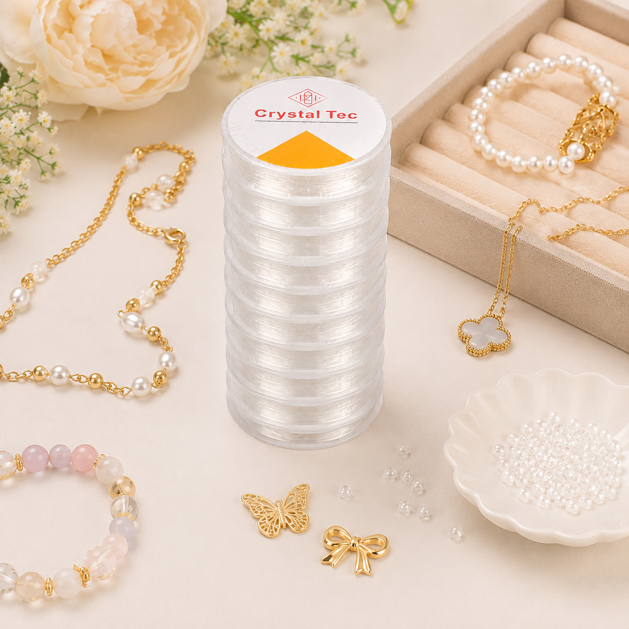 A stack of clear plastic spools of thread or cord labeled Crystal Tec, styled on a light beige surface with jewelry props including pearl bracelets, gold-tone necklaces, beads, and a flower box.