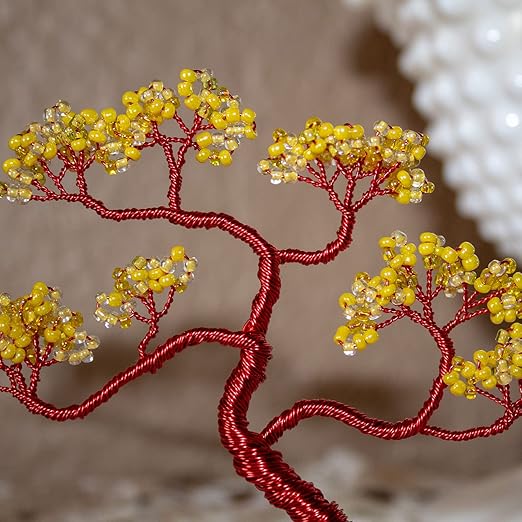 A close-up of a decorative wire tree with red wrapped branches and clusters of small yellow and clear faceted beads, shown against a soft beige background.