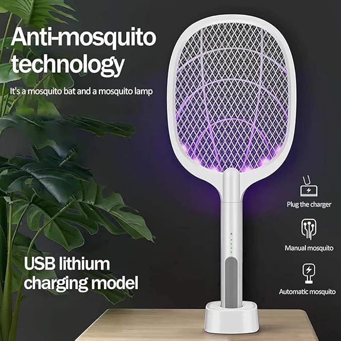 White anti-mosquito electric fly swatter lamp with built-in LED purple light, shown on a stand on a wooden surface with a dark background, green plant leaves on the left, and feature text including 'Anti-mosquito technology' and 'USB lithium charging model'.