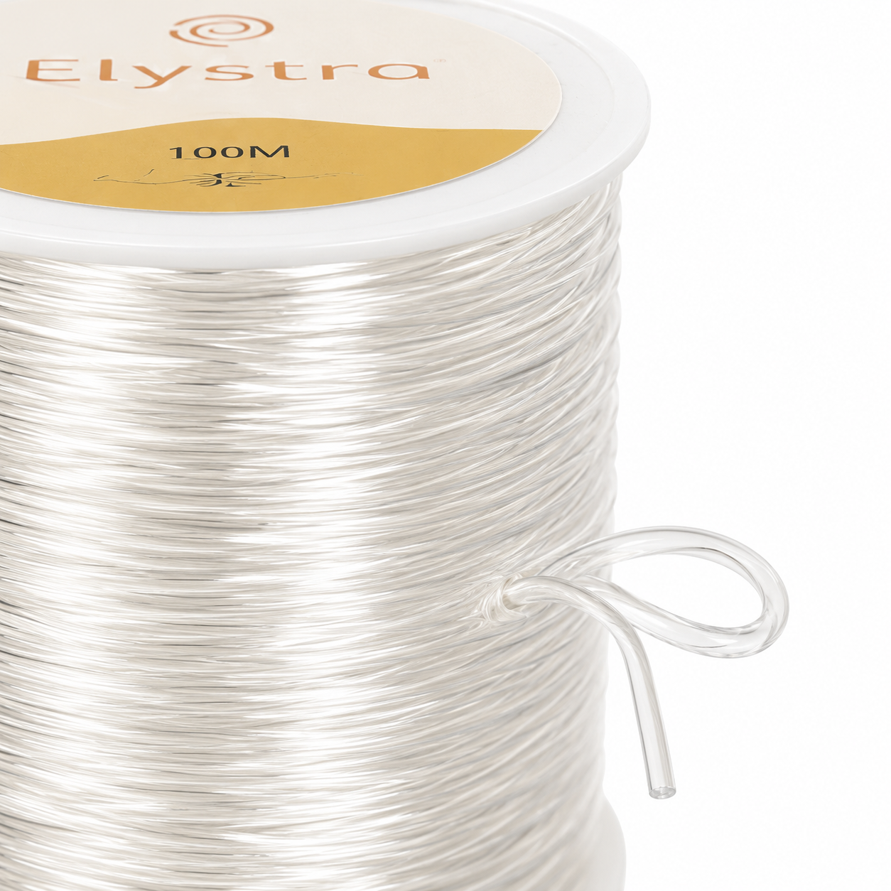 A close-up of a spool of Elystra 100M clear elastic cord, showing the white plastic spool, the clear thread wound around it, and a small loop of the cord extending from the side.