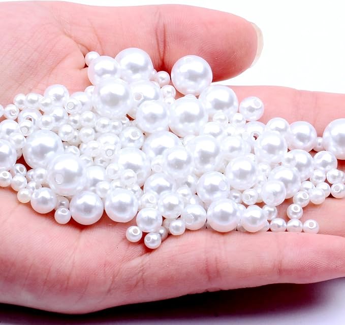 A hand holding a pile of white faux pearl beads in various sizes against a plain white background.