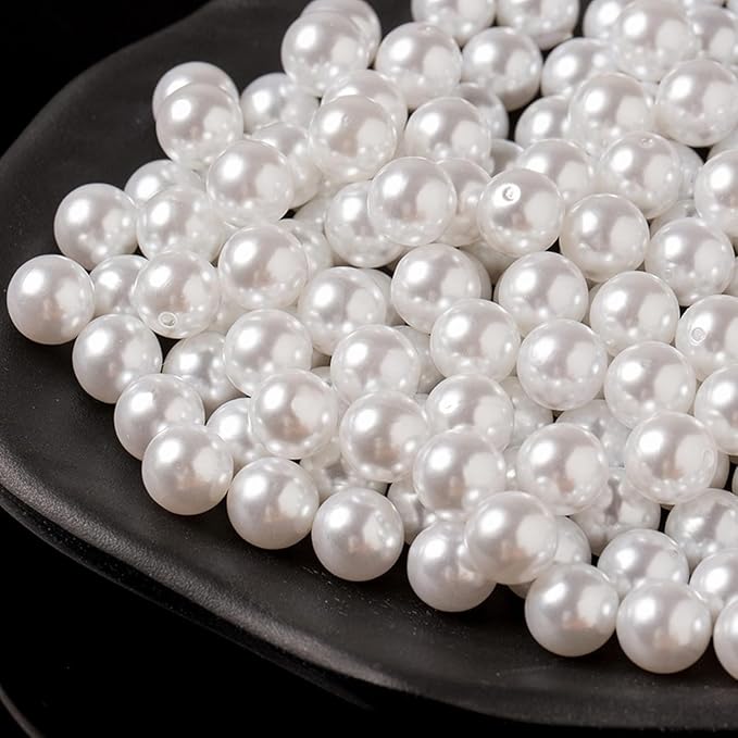 A pile of white faux pearl beads with a glossy, lustrous finish, arranged on a black plate against a dark background.